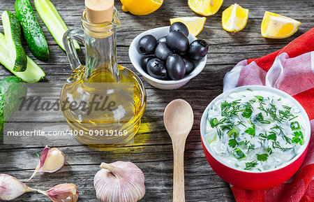 Tzatziki, cucumber, bottle of olive oil on an old wooden table against the background of a cutting board
