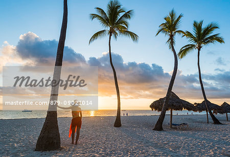 Bavaro Beach, Bavaro, Higuey, Punta Cana, Dominican Republic. Woman admiring the sunrise on a palm-fringed beach (MR).