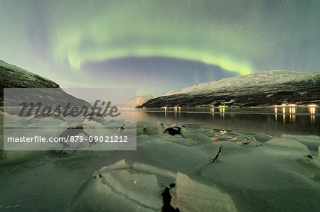 Northern Lights reflected in the cold sea frames the rocks covered with ice Manndalen Kafjord Lyngen Alps Tromsø Norway Europe