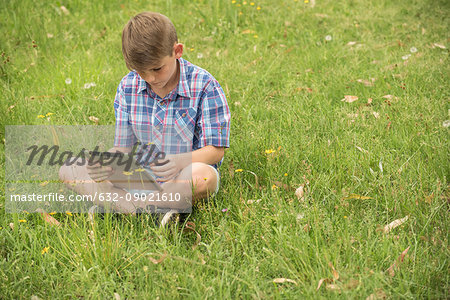 Boy sitting on grass, using digital tablet