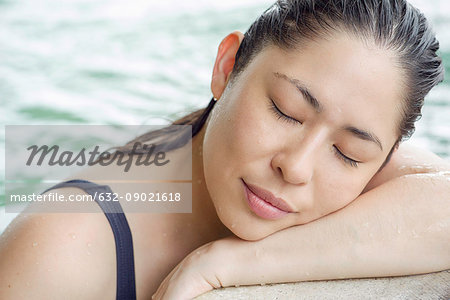 Woman at side of swimming pool resting head on arms