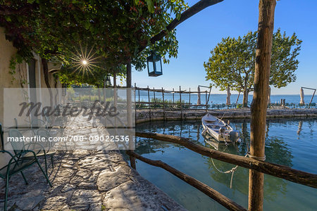 Sun shining on the stone patio at Locanda San Vigilio overlooking a little harbor and Lake Garda in the morning at Punta San Vigilio in Garda, Veneto, Italy