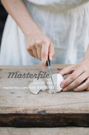 Woman slicing mozzarella on chopping board, mid section
