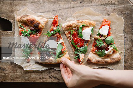 Woman taking pizza slice from chopping board, overhead view