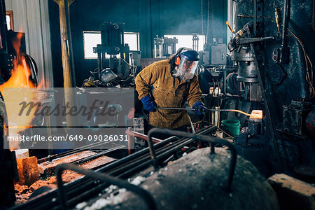 Blacksmith shaping red hot metal rod in workshop