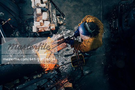 Overhead view of blacksmith shaping red hot metal rod in workshop furnace
