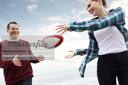 Father and daughter playing rugby on beach