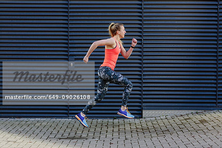 Young female runner speed running along sidewalk