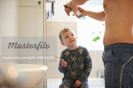 Boy in bathroom with father preparing to brush teeth