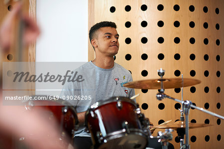 Young male college student playing drums in recording studio