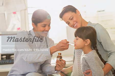 Female pediatrician feeding cough syrup to girl patient in examination room