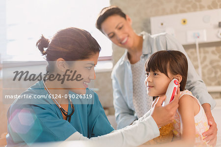 Female nurse using digital thermometer in ear of girl patient in examination room