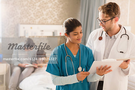 Doctor and nurse making rounds in hospital, reviewing medical record on clipboard