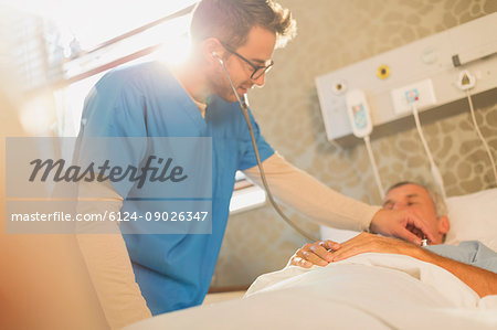 Male nurse using stethoscope on patient in hospital bed