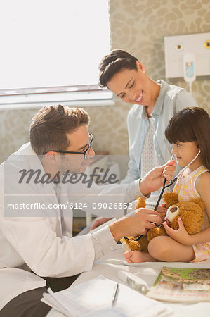 Male doctor showing stethoscope to girl patient in hospital room