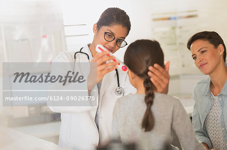 Female doctor using digital thermometer in ear of girl patient in examination room