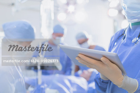 Surgeon wearing rubber gloves, using digital tablet in operating room