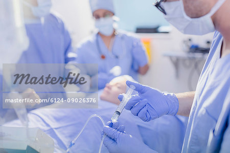 Anesthesiologist with syringe injecting anesthesia into IV drip in operating room