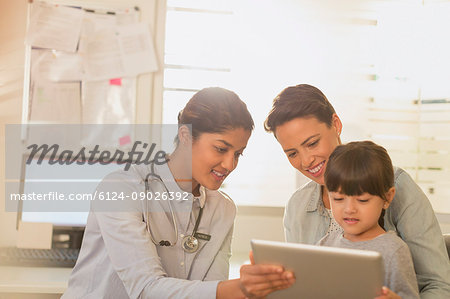 Female pediatrician showing digital tablet to girl patient and mother in examination room