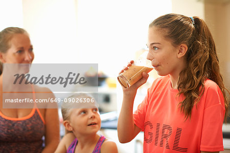 Teenage girl drinking glass of fresh smoothie in kitchen