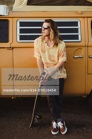 Young male skateboarder leaning against vintage recreational vehicle, Exeter, California, USA