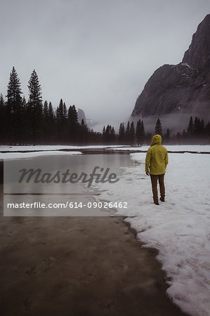 Rear view of male hiker looking out over snow covered landscape and river, Yosemite Village, California, USA