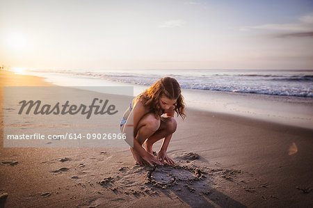 Girl drawing heart in sand on beach