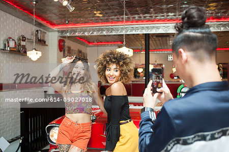 Three friends in diner, young man taking photograph of female friends, using smartphone