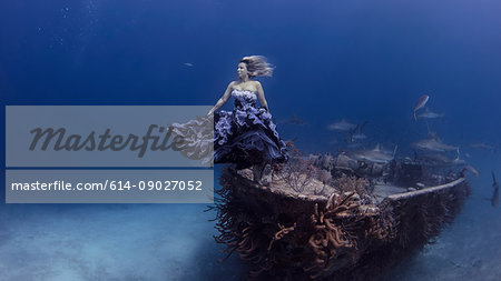 Underwater view of woman in purple dress poised by shipwrecked boat, Bahamas