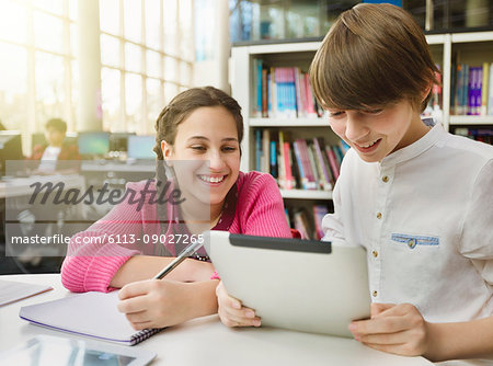 Smiling students researching, using digital tablet at table in library