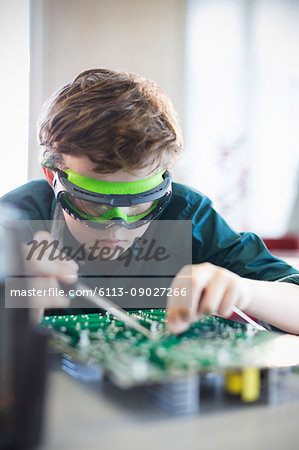 Focused boy student in goggles soldering circuit board in classroom