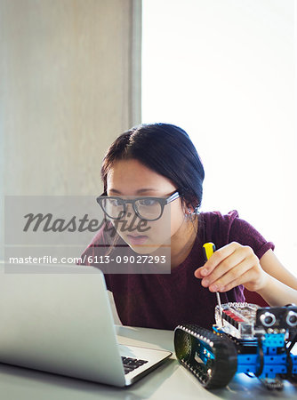 Focused, curious girl programming and assembling robotics at laptop in classroom