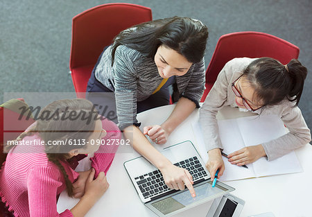 Female teacher helping girl students researching at laptop at library table