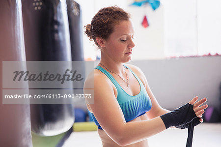 Female boxer wrapping wrists next to punching bag in gym