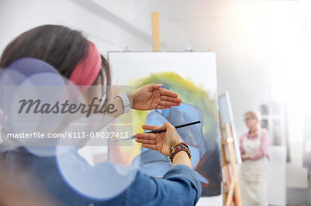 Female artist gesturing, framing painting on easel in art class studio