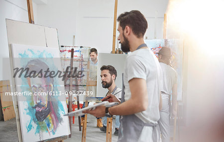 Male artists painting at easel in art class studio