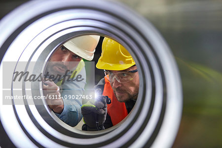 Serious male engineers with flashlights examining steel pipe