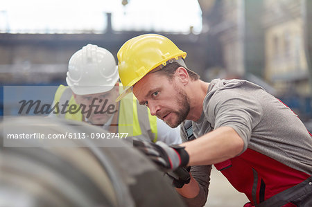 Focused male engineers examining steel part in factory