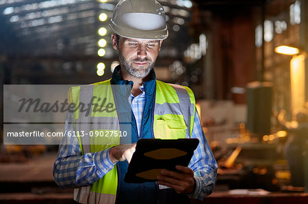 Male engineer working at glowing digital tablet in dark factory