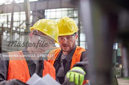 Male workers discussing paperwork in factory