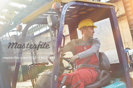 Male worker driving forklift, backing up in factory