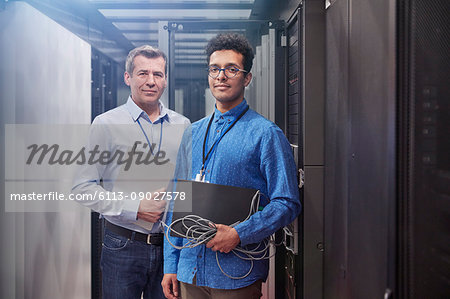 Portrait confident male IT technicians with laptop and clipboard in server room