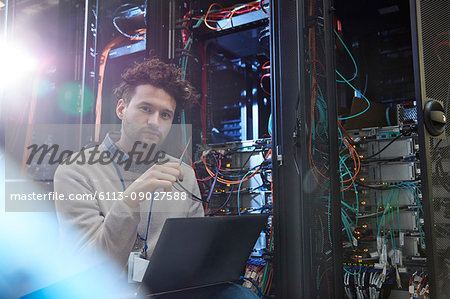 Portrait confident male IT technician working at laptop in server room