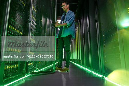 Male IT technician working in dark server room with glowing green panels