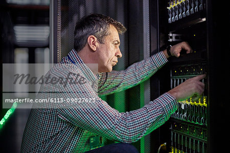 Focused male IT technician working at panel in dark server room