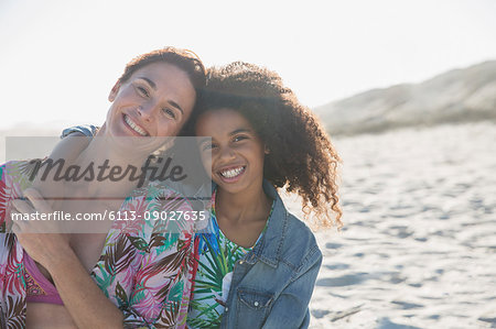 Portrait smiling, confident mother and daughter hugging on sunny, summer beach