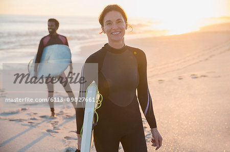 Portrait confident woman in wet suit with surfboard on sunny summer beach with family