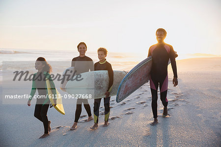 Family surfers carrying surfboards on summer sunset beach