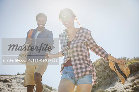 Smiling, affectionate multi-ethnic couple holding hands walking on sunny summer sand beach path