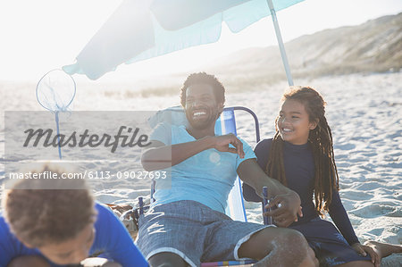 Laughing father and children relaxing on sunny summer beach